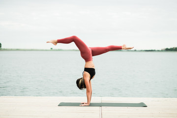 young girl doing yoga outdoors on the pier by the lake.