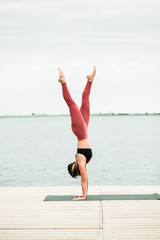 young girl doing yoga outdoors on the pier by the lake.