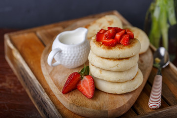 mini stack of cheesecakes on wooden tray, with slices of strawberries, sauce on table