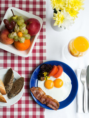 breakfast, eggs with bacon and fresh vegetables, orange juice, fruit, on table