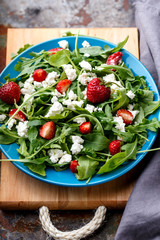 Salad with arugula, strawberries, cottage cheese, olive oil, on a small plate, wooden board and rusty background