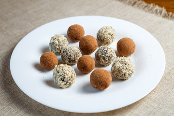 Homemade candy in the form of balls of dried fruit with walnut and cocoa powder on a white plate on a linen napkin on the table. Healthy food without sugar and gluten.