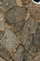 The texture of the sidewalk of chaotic granite stones of different colors with many cracks