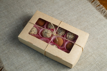Homemade candy in the form of balls of dried fruit with walnut and cocoa powder in the box on a linen napkin on the table. Healthy food without sugar and gluten.