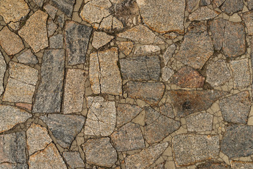 The texture of the sidewalk of chaotic granite stones of different colors with many cracks