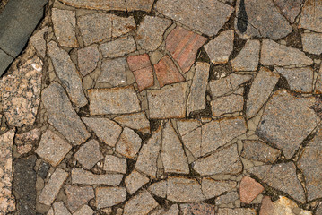 The texture of the sidewalk of chaotic granite stones of different colors with many cracks