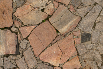 The texture of the sidewalk of chaotic granite stones of different colors with many cracks