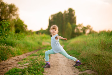 Fototapeta na wymiar Little girl doing fitness exercises outdoor at surise