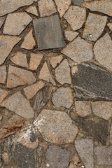 The texture of the sidewalk of chaotic granite stones of different colors with many cracks
