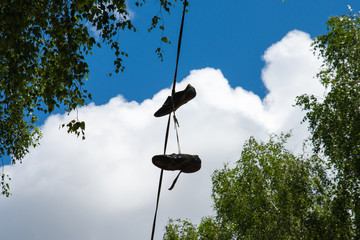 Old sneakers hanging on wires in the summer on a background of clouds and branches of birch trees