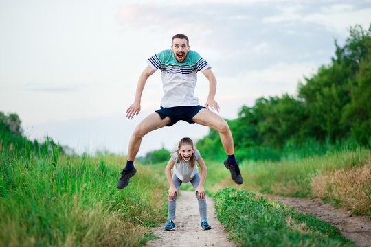 Sport family portrait of handsome father and his cute little daughter play leap frog outdoor at sunset