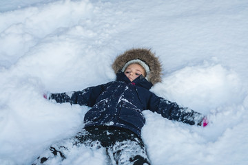 Fototapeta na wymiar Little girl lying in a deep snow