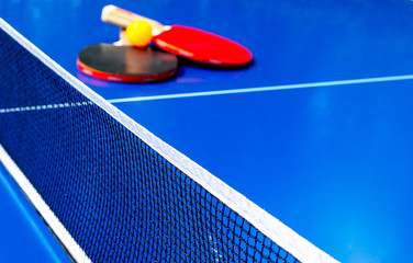 Blue table tennis or ping pong. Close-up ping-pong net. Close up ping pong net and line. Two table tennis or ping pong rackets or paddles  and ball on a blue table with net background