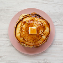 Homemade pancakes with butter and maple syrup on a pink plate on a white wooden surface, top view. Overhead, flat lay, from above. Close-up.