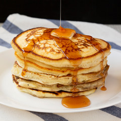 Homemade pancakes with butter and maple syrup on a white plate, side view. Close-up.