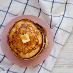 Homemade pancakes with butter and maple syrup on a pink plate, overhead view. Flat lay, top view, from above.