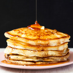 Homemade pancakes with butter and maple syrup on a pink plate, side view. Closeup.