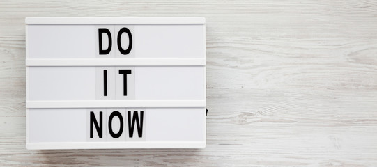 'Do it now' words on a modern board on a white wooden surface. Flat lay, overhead, top view. Space for text.