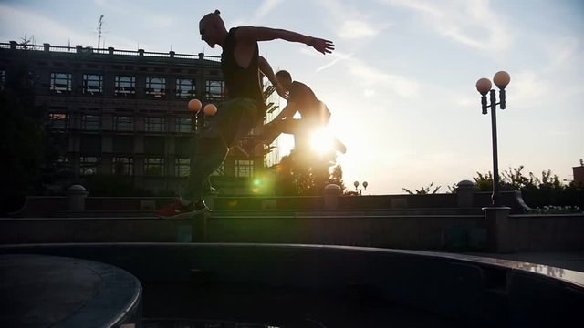 Two acrobatic men running up and jump over the fountain - sunset