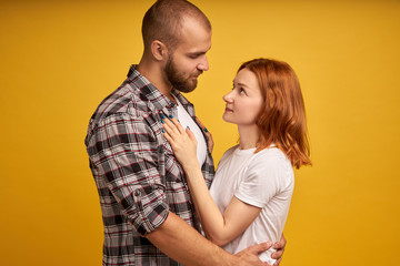 Photo of cheerful lovely family coupe cuddle each other, have fun together, look with big love and affection, wear stylish clothes, isolated over yellow background. People and closeness concept