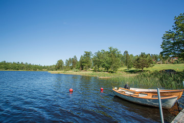 Fototapeta na wymiar View of lake with two boats parked in shore on blue sky background. Beautiful nature landscape backgrounds. 