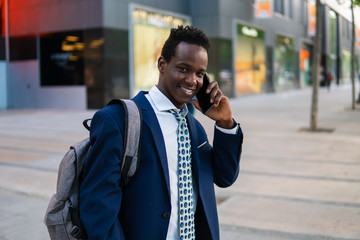 African American businessman holding mobile phone wearing blue suit and using modern smartphone near office. Business concept