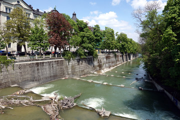 The fast river Isar edged by stone embankment with a lot of tree trunks stuck in the rapids in Munich city on a sunny spring day