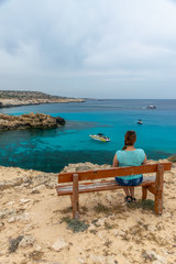 CYPRUS - MAY 11/2018: Tourist sits on a wooden bench near the blue lagoon.