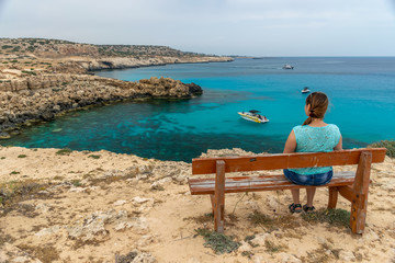 Fototapeta premium CYPRUS - MAY 11/2018: Tourist sits on a wooden bench near the blue lagoon.