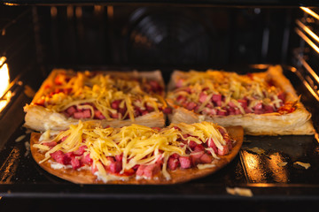 Homemade pizza in the oven close-up, sausage sprinkled with cheese