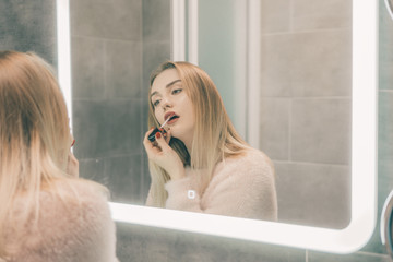 The girl in the bathroom in front of the mirror paints her lips.