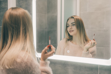 The girl in the bathroom in front of the mirror paints her lips.