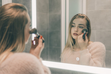 The girl in the bathroom in front of the mirror is painting.