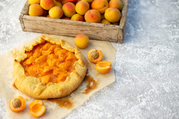 Homemade fruit pie (galette) made with fresh organic apricotes, top view. Open pie, apricot tart. Fruit bakery. Summer food, summer pie on parchment paper. Wooden box with apricots.