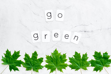 Go green text with green maple leaves on marble background top view