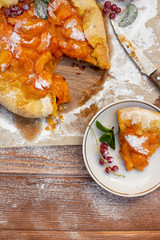 Homemade fruit pie (galette) made with fresh organic apricotes with powdered sugar on wooden table, top view. Plate with a cut piece of cake. Open pie, apricot tart. Summer pie on parchment paper.