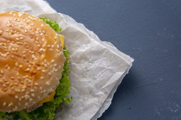 Burger with beef patty, salad, a slice of tomato and cheese, onions and sauce with paprika in a grilled bun with sesame