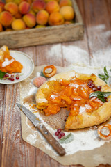 Homemade fruit pie (galette) made with fresh organic apricotes with powdered sugar on wooden table, top view. Plate with a cut piece of cake. Open pie, apricot tart on parchment paper.