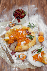 Homemade fruit pie (galette) made with fresh organic apricotes with powdered sugar on wooden table, top view. Plate with a cut piece of cake. Open pie, apricot tart on parchment paper.