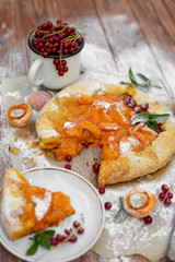 Homemade fruit pie (galette) made with fresh organic apricotes with powdered sugar on wooden table, top view. Plate with a cut piece of cake. Open pie, apricot tart on parchment paper.