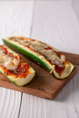 Two fresh hot zucchini boats with red sauce and melted cheese on cutting board.