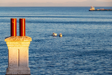 Two blurred fishing boats and a container ship behind a sunlit chimney at the Europa Point Lighthouse, Gibraltar