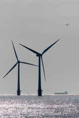 Clean energy production development. Offshore wind power turbine silhouette with supply vessel.