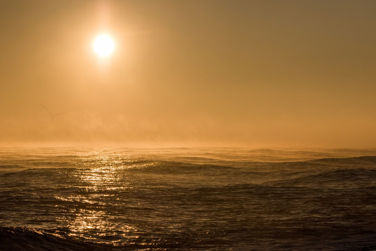 Seascape sunrise. Beautiful misty morning sun over sea with background wind turbine.