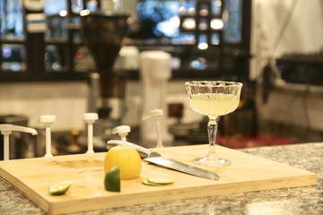 Cocktail with lemon, yellow color, glass, on the bar with wood plate and knife