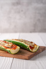Two fresh hot zucchini boats with red sauce and melted cheese on cutting board.