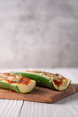 Two fresh hot zucchini boats with red sauce and melted cheese on cutting board.