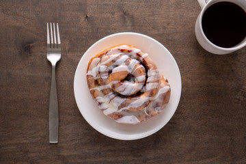Large gourmet frosted cinnamon roll on brown distressed table.