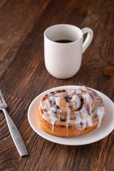 Large gourmet frosted cinnamon roll on brown distressed table.