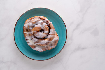 Large gourmet frosted cinnamon roll on marble table.